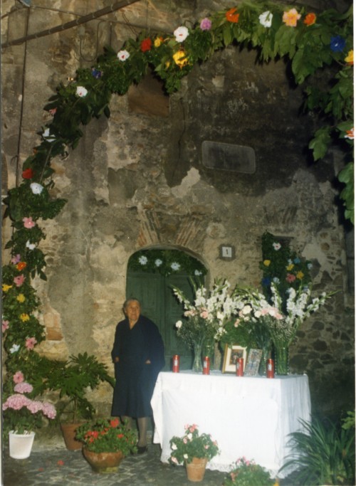 Anziana circondata da un allestimento di fiori e vicino un altare in onore della Madonna Addolorata