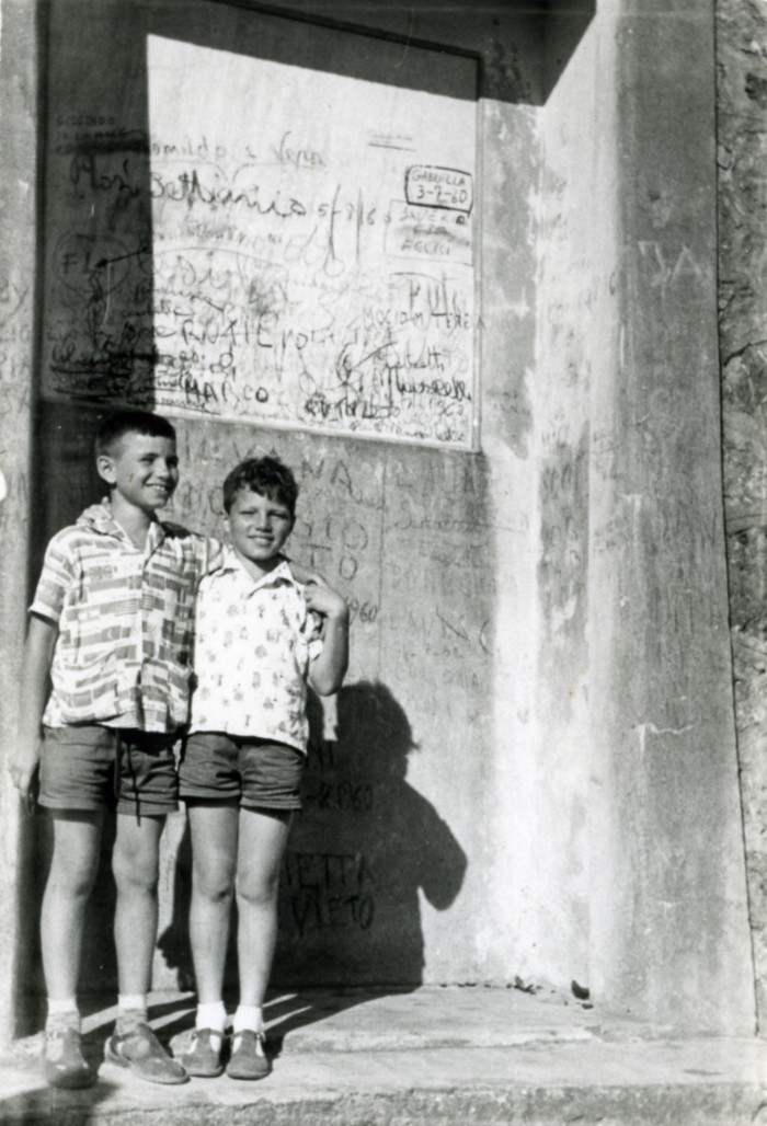 Due bambini abbracciati davanti a un muro con scritte e graffiti