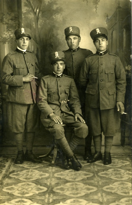 Giacomo Rocchi e altri tre ragazzi, in divisa da militari, in studio con fondale dipinto. Uno di loro è seduto