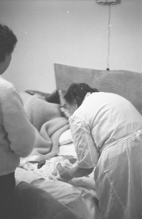 Levatrice di spalle veste il neonato con sulla sinistra una donna che osserva la scena