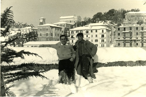 Due uomini con la neve con sullo sfondo i palazzi di Tolfa