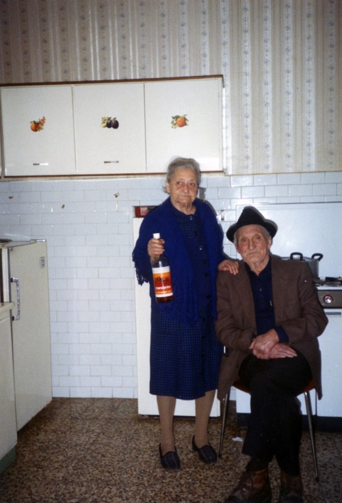 Un uomo e una donna nella cucina di casa. L'uomo è seduto su una sedia, mentre la donna tiene in mano una bottiglia